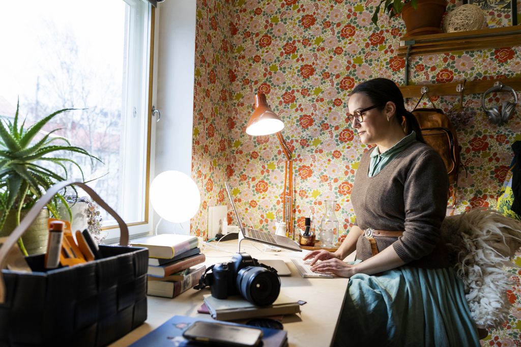 Hanne Valtari istuu kotonaan työpöydän ääressä ja kirjoittaa tietokoneella