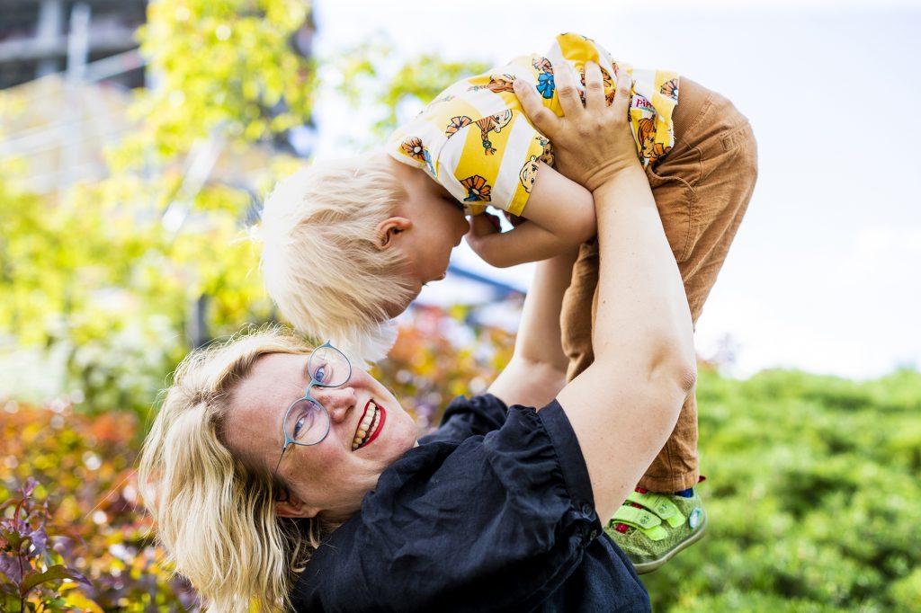 Kuvassa Jenni Gästgivar nostaa poikaansa päänsä ylle ja hymyilee kameralle.