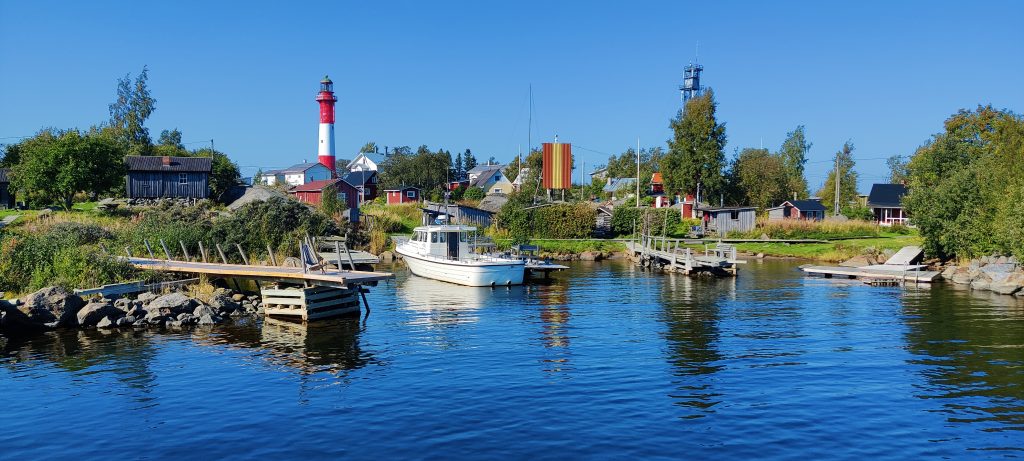 Kuvan alalaidassa on tyyntä merta, joka nuolee rannan laitureita ja yksinäistä kalasajavenettä. Päivä on kirkas ja meri tyyni, satama on suojaisa. Rannassa on vanhoja kalastajatupia, venevajoja ja tyrnipensaita. Koko saari on profiililtaan melko matala. Kauempana kohoava Tankarin majakka on rungoltaan pyöreä ja väreiltään punavalkoinen. Sen valo ohjaa yhä merenkulkijoita.